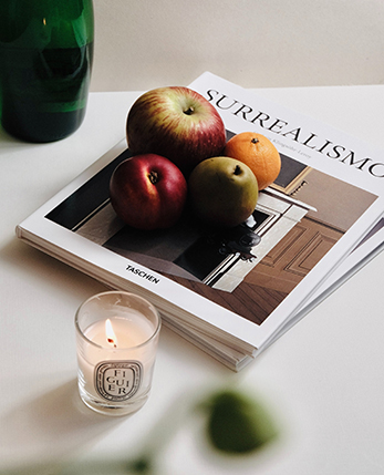 Stack of magazines next to vase and candle on white table.